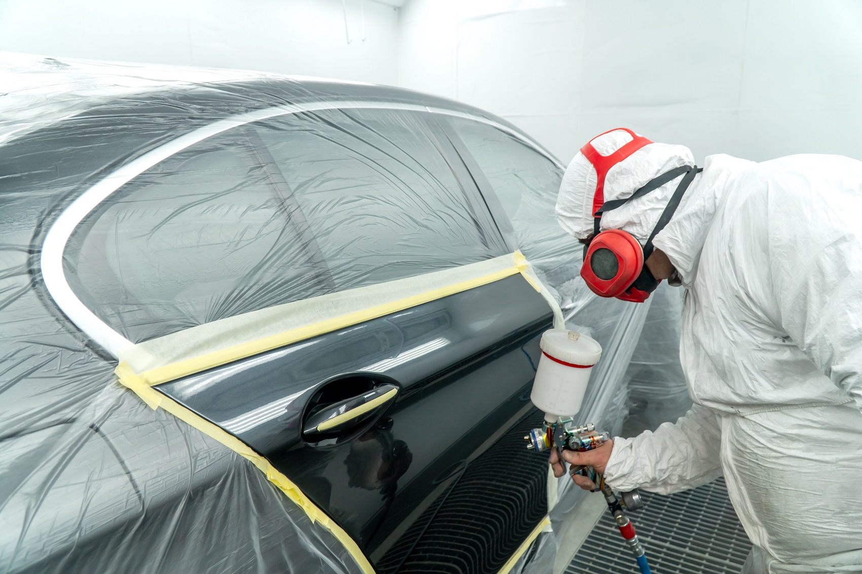 Technician painting a car with a spray gun in a paint booth